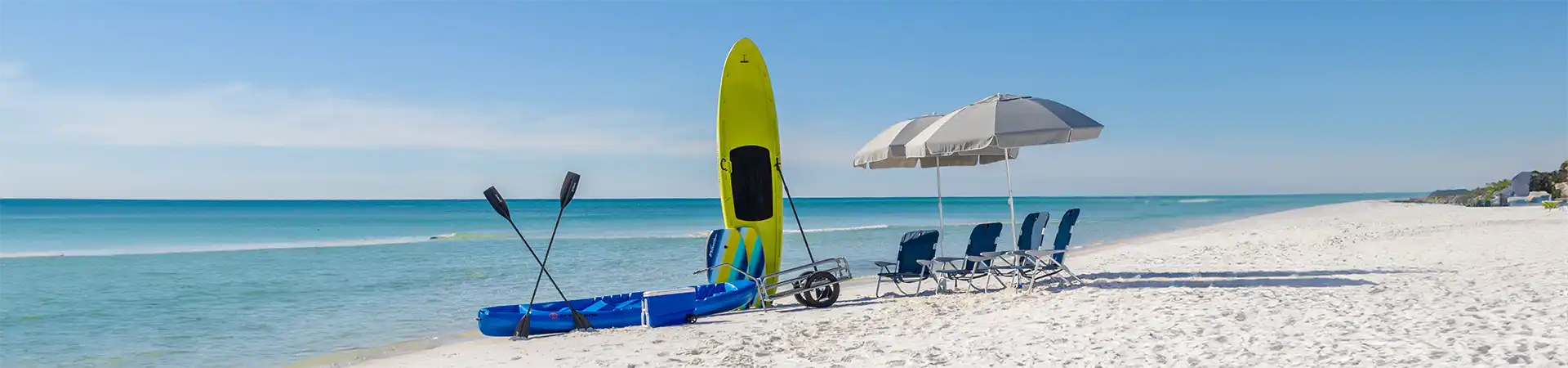 beach chairs under a beach umbrella, next to kayak, SUP and cooler